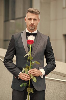 Siyah smokinli zarif bir adam. Smokin papyon takan adam dışarıda. Kırmızı güllü beyaz smokinli adam..