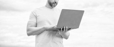 Gökyüzü arka planında dizüstü bilgisayarda çalışan adamın kırpılmış görüntüsü.