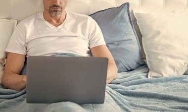 Yatakta dizüstü bilgisayarda çalışan meşgul bir adam..