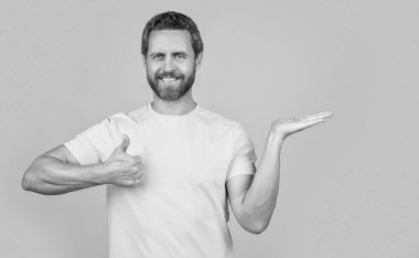 Reklam sunan gülümseyen adamın fotoğrafı, başparmağınızı kaldırın. Sarı üzerine izole edilmiş reklam sunan adam. Adam arka planda reklam sunuyor. Stüdyoda reklam sunan adam..