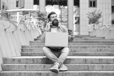 Cep telefonuyla konuşan, merdivenlerde kahve içen mutlu adam. Gülümseyen adam dışarıda dizüstü bilgisayar kullanarak cep telefonu görüşmesi yapıyor. Mobil iletişim. Telefon görüşmesi. Cep telefonu çağrısı.