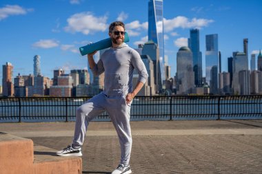 New York 'ta sporcu. Manhattan 'da spor kıyafetli bir adam. Vücuduna uygun. Yoga koçu. Sporcu adam antrenmana hazır. Sağlıklı bir yaşam tarzı. Spor ve spor. Eğitim için yoga minderi. Güneşli bir gün.