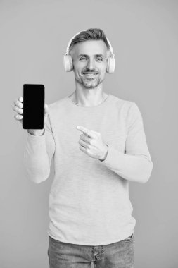 Point finger on phone screen. Music lifestyle. Audio playlist. Mature man in headphones. Man in headphones choosing playlist of mp3 on phone. Man using phone application isolated in blue. Copy space. clipart