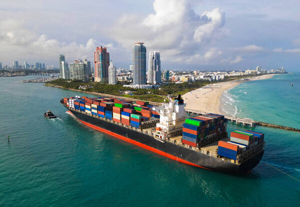 Экспорт и импорт. Грузовой бизнес. Порт Майами. Грузовой корабль с контейнером в Майами, антенна. Грузовой контейнер на грузовом корабле. Грузовое судно покидает порт. Контейнерный корабль. Линия жизни морской торговли