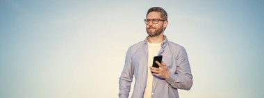 Gözlüklü adam akıllı telefondan fotokopi odasıyla sohbet ediyor. Adam telefonda mesajlaşıyordu. Akıllı telefon iletişimi. Adam gökyüzü arka planında sohbet ediyor.