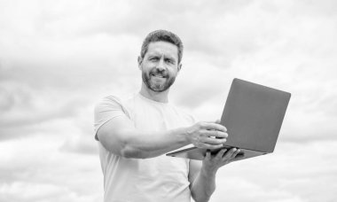 smiling man working online on laptop on sky background.
