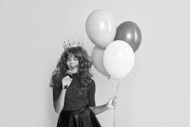 cheerful child in crown with microphone and party balloon on yellow background.