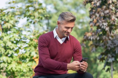 Adam sonbahar parkında telefon kullanıyor. Sıradan bir iş adamı gibi. İş adamı dışarıda telefonla mesajlaşıyor. İş iletişimi tarzı. Çevik iş. İnternet işi. İşadamı sonbaharda telefon kullanır..