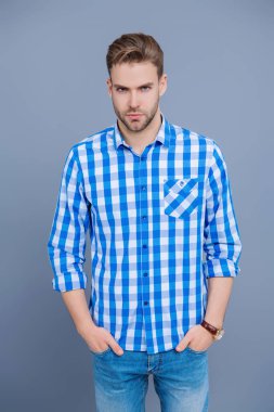 Tıraşsız adamın zarif portresi. Gri yolda izole edilmiş bir adam. Kareli gömlek giyen milenyum adamı. Milenyum erkeğinin gündelik tarzı. Sıradan tişörtlü bir adamın portresi. Çabasız bir şekilde şık..