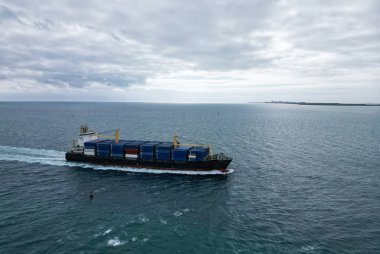 Kargo gemisi denizde, hava manzaralı. Yük konteynırı kargo gemisine yüklendi. Hava görüntülü kargo gemisi limana giriyor. Kargo işi. Deniz kenarındaki konteynır gemisi. Nakliye lojistiği. Ticari nakliye.