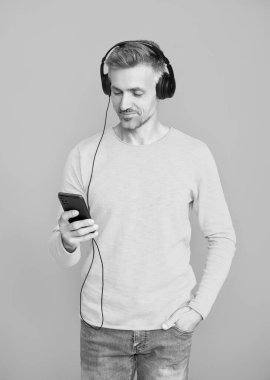 Kulaklıklı adam telefonda mp3 çalma listesini seçiyor. Telefon uygulamasını mavi kullanan bir adam. Telefonla müzik dinlemek. Müzik yaşam tarzı. Ses çalma listesi. Kulaklık takan olgun bir adam. Elektronik aygıt.