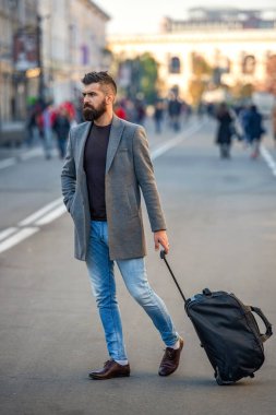 Sakallı şık bir adam şehir caddesinde seyahat çantası ya da bavuluyla iş seyahatine çıkıyor, iş adamı seyahat ediyor..