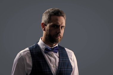 Yakışıklı, karizmatik garson smokin giyer, şık papyon giyer ve gri renkte klasik üniforma giyer..