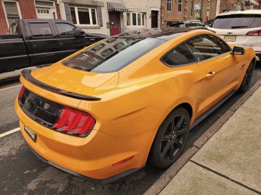 New York City, ABD - 10 Mart 2024: 2018 Ford Mustang sarı spor arabası, köşedeki manzara.