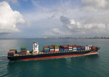 Yük konteynırı kargo gemisine yüklendi. Hava görüntülü kargo gemisi limana giriyor. Kargo işi. Konteyner gemisi. Nakliye lojistiği. Liman operasyonları. Kargo gemisi denizde, hava manzaralı..