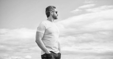 Sarı gömlekli ve güneş gözlüklü sakallı adam gökyüzü arka planında..