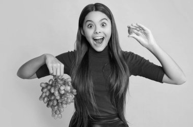 surprised girl hold fresh grapes fruit on yellow background.