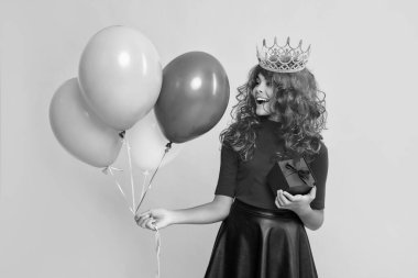 sarı arka planda hediye kutusu ve parti balonuyla taç giymiş sürpriz bir çocuk..