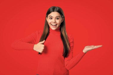 Ürünü baş parmağınla sunuyorsun. Kırmızıda izole edilmiş genç bir kızın portresi. Genç kız kameraya bakıyor. Sıradan bir tarz. Tarz sahibi kızın uzun saçları var. Genç tek renkli moda tarzında. Kız için biçim.