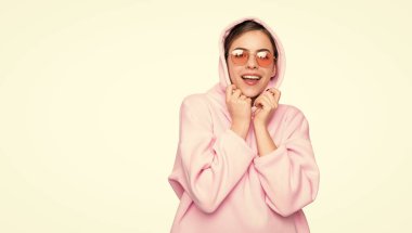 Şık gözlüklerle gülümseyen mutlu moda kızı ve beyaza izole edilmiş pembe kapüşonlu kapüşonlu sweatshirt..