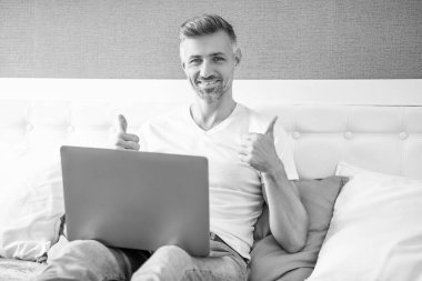 Yetişkin bir adam dizüstü bilgisayarla yatakta çalışıyor. başparmak yukarı.