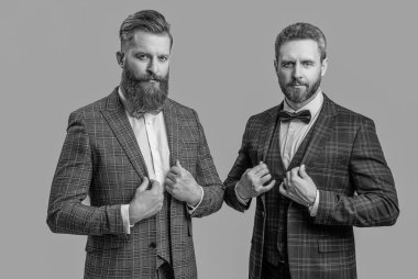 Erkek giyim bölümünde smokin giyen adamlar. Smokinli erkekler erkek giyim tarzı giyinir. Papyonlu şık giyinen şık adamlar. İş etkinliğindeki iki iş adamı. Smokinli adamlar gri alanda izole edilmiş. Klasik terzilik.