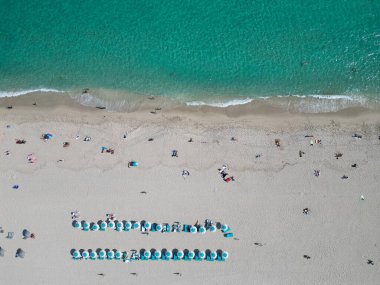 Yazın deniz kenarında tatil. Deniz, plaj şemsiyesi altında rahatlar. Denize açılın. Kristal berrak turkuaz suyla kumsalın havadan görünüşü. Cennette yaz tatili.