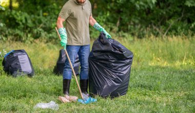 Çevre gönüllüsü. Ormanda çöp toplama. Ekoloji konsepti. Çöp toplama gönüllüsü, ekoloji. Çöp torbasıyla lastik eldivenli adam çöpü temizliyor. Adam plastik çöp topluyor. Ev atıkları.