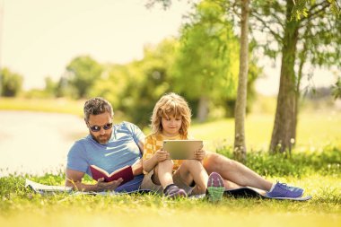 çocukluk okulu eğitimi. Oğlu ve babası yazın kaynaşıyorlar. Baba ve oğul eğitimi. Baba oğul eğitimini kitap ve tabletle şekillendirir. Baba ve oğul parkta rahatlayın. açık havada öğrenme.