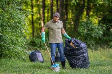 Ormanda çöp toplama. Ekoloji konsepti. Çöp toplama gönüllüsü, ekoloji. Çöp torbasıyla lastik eldivenli bir adam çöpü temizliyor. Adam plastik çöp topluyor. Çevre gönüllüsü. Geri dönüşüm.