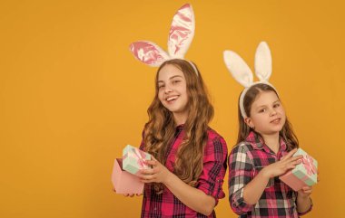 Tavşan kulaklı gülümseyen Paskalya çocukları hediye kutusunu fotokopi alanı ile sarı arka planda tutun.