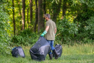 Ekoloji konsepti. Çöp toplama gönüllüsü, ekoloji. Çöp torbasıyla lastik eldivenli adam çöpü temizliyor. Adam plastik çöp topluyor. Çevre gönüllüsü. Ormanda çöp toplama. Atık yönetimi.