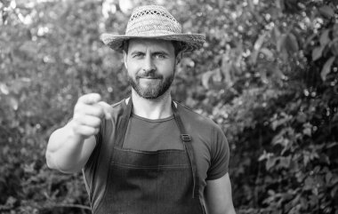 Çiftçi şapkalı ve önlüklü mutlu çiftçi açık havada parmağını öne uzatıyor..