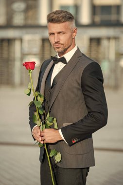 Sevgililer Günü konsepti. Sevgililer Günü gülü olan gri siyah smokinli adam. Sevgililer Günü için çiçek hediyesi.