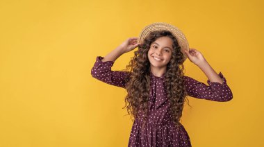 Hasır şapkalı mutlu çocuk, sarı arka planda uzun sarı kıvırcık saçlı..