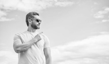 Sarı tişörtlü ve güneş gözlüklü adam gökyüzünü işaret ediyor..