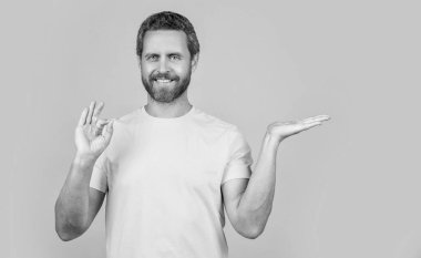 Stüdyoda reklam sunan neşeli adam, tamam. Reklam sunan adamın fotoğrafı. Sarı üzerine izole edilmiş reklam sunan adam. Adam arka planda reklam sunuyor..