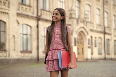 Eğitim ve bilgi. Okul çantası takan ve egzersiz kitabı tutan öğrenci kız. Açık hava ilkokulu mutlu genç kız portresi. Gözlüklü kız öğrenci. Okula dönelim. Öğrenci geliştirme.