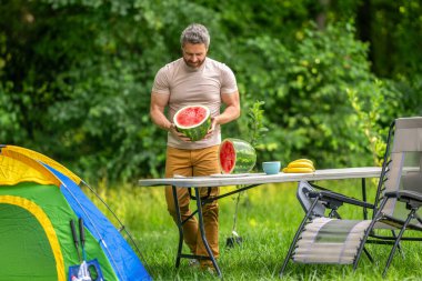 İspanyol adam kamp yapıyor. Karpuz kampı pikniği. Lezzetli sağlıklı yiyecekler. Kampta taze yiyecek. Yaz kampında karpuzlu bir adam. Yaz günü doğa yürüyüşçüsü. Kamp ve doğa pikniği.
