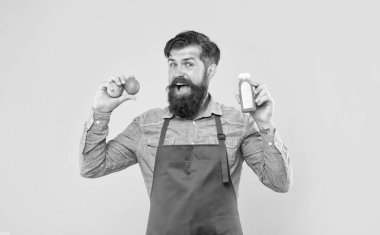 Happy man in apron holding limes and juice bottle yellow background, juice barman.