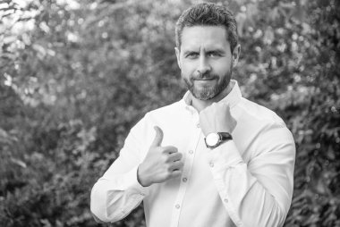 Professional man giving thumbs up showing wristwatch natural background, punctuality.