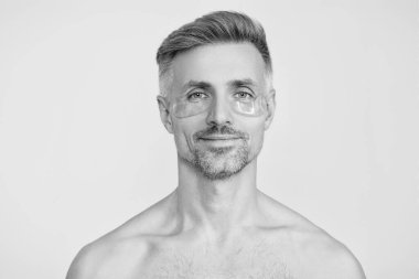 Göz bandı. Göz altlarında kolajen pedleri olan bir güzellik uzmanı. Olgun bir adamın gözlerinin altında kolajen bantları olan taze ve sağlıklı bir cildi vardır. Yüz bakımı. Göz bandı takan bir adam. Spa bakımı. Cilt rutini.