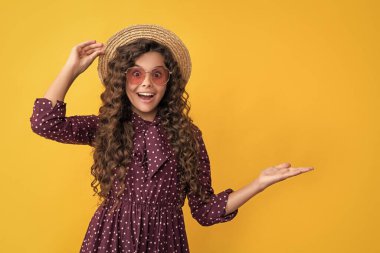 surprised happy child in straw hat and sunglasses with long brunette curly hair. copy space.