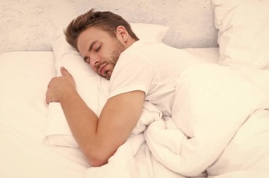 Genç adam uyuyor ya da beyaz yatak odasında evinde uyuyor..