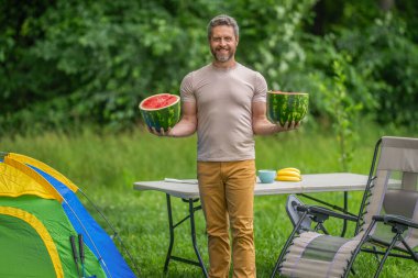 Kamp ve doğa pikniği. Adam kampı. Karpuz kampı pikniği. Lezzetli sağlıklı yiyecekler. Kampta taze yiyecek. Yaz kampında karpuzlu bir adam. Yaz günü doğa yürüyüşçüsü. Mutlu yaz..