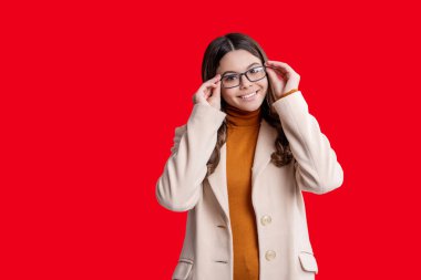 Moda ve şık bir öğrenci kız gülümsüyor. Gençler için sonbahar moda tarzı. Sonbahar modası. Sonbahar montlu kız öğrenci kırmızıda izole edilmiş. Genç kız gözlük takıyor. Sonbahar stil kızı. Boşluk afişini kopyala.