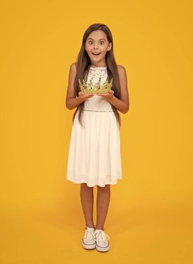 amazed teen child in crown on yellow background.