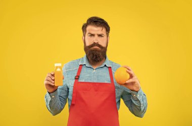 Elinde turuncu ve meyve suyu şişesi olan ciddi bir adam sarı arka planda, barmen..