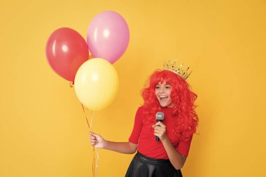 Sarı arka planda mikrofonlu ve parti balonlu mutlu çocuk..