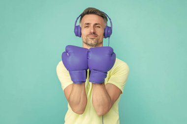 Boks eldivenli sporcu mavi üzerine izole edilmiş. Kulaklık takan olgun bir boksör. Sporcu boks. Güçlü adam müzik dinler. Spor salonundaki sporcu. Spor giyim bölümünde boksör. Egzersiz ve yumruk. Boks eldivenleri.